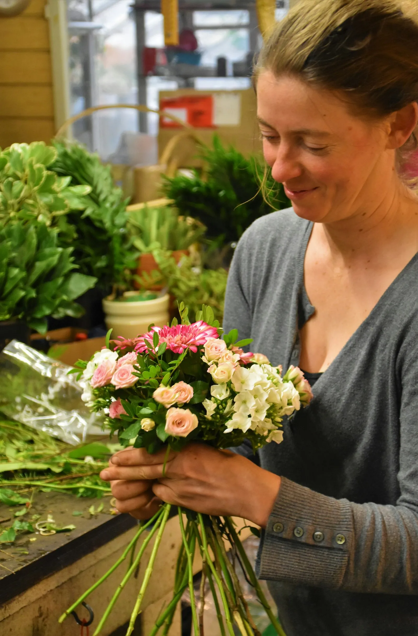 A florist arranging a bouquet of pink and white flowers in her shop